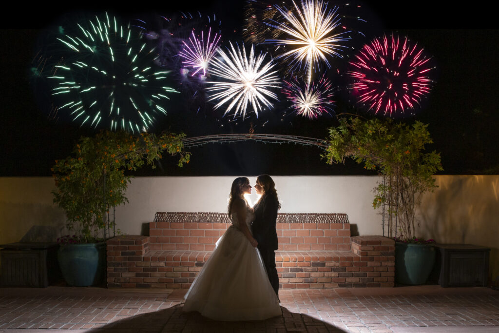 Romantic wedding moment under a vibrant fireworks display, featuring a newlywed couple silhouetted against a glowing night sky.