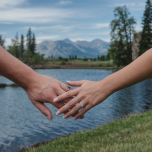 A romantic shot of a couple holding hands near a lake, with a mountain range in the background, showcasing love and engagement photography ideas in a natural setting.